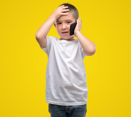 Canvas Print - Dark haired little child using a smartphone stressed with hand on head, shocked with shame and surprise face, angry and frustrated. Fear and upset for mistake.