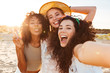 Three positive multiethnic women 20s in summer clothing smiling at camera, while taking selfie photo during holiday on nature