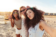 Three joyful multiethnic women 20s in summer clothing smiling at camera, while taking selfie photo during beach party