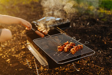 Close Up Of Woman's Hand Grilling Sausages And Bacon Strip On Barbeque Grill