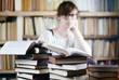 © Sinuswelle - Woman in the Library with piles of Books - junge Frau in einer Bibliothek studiert die Bücher
