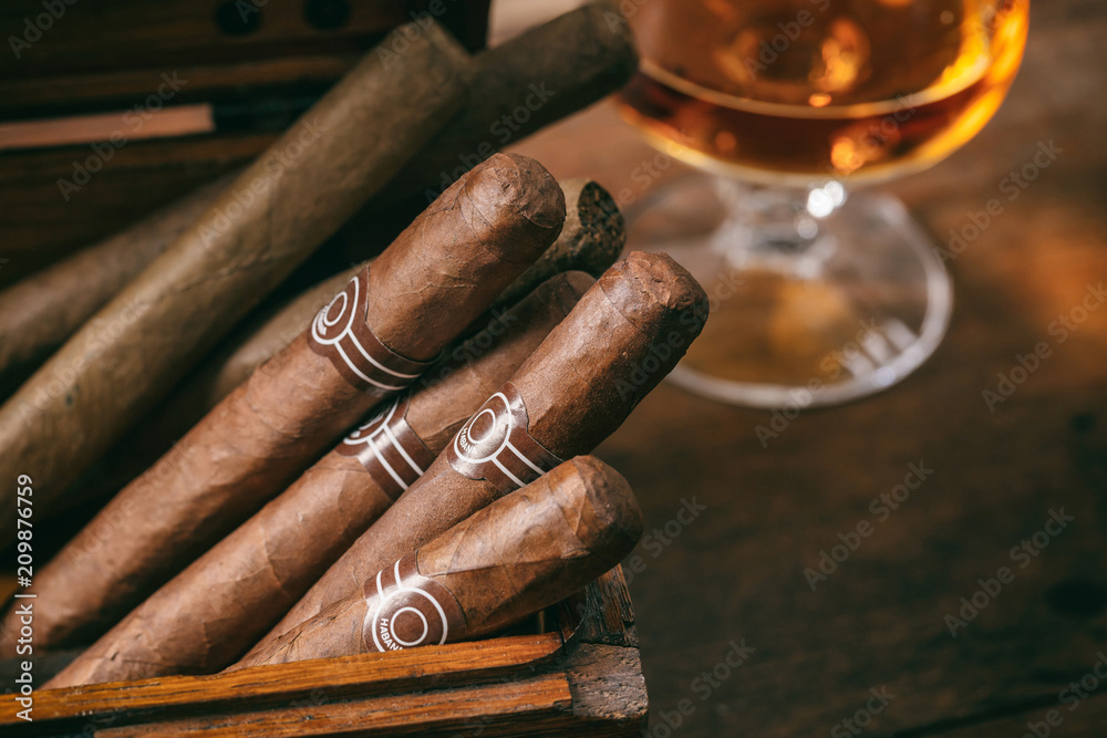 Cuban cigars closeup on wooden desk, blur glass of brandy - obrazy, fototapety, plakaty 