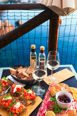 Wall Mural - Romantic dinner for two at sunset. White wine and Tasty italian snack: fresh bruschettes  and meat on the board in outdoor cafe with amazing view in Manarola