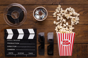 Clapperboard, film reel and popcorn on wooden background, top view