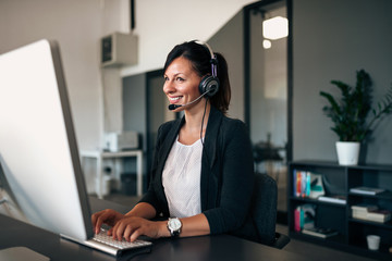 Canvas Print - Beautiful customer representative with headset smiling during conversation with a client.