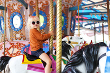 Cute Little Toddler Girl In Big Sunglasses Riding On Carnival Carousal