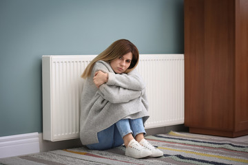 Wall Mural - Sad woman suffering from cold on floor near radiator