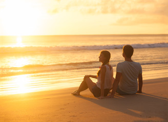 Wall Mural - sunset silhouette of young couple in love sitting at beach