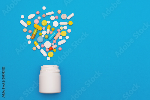 Fotografia Assorted medical pills and capsules scattered from a bottle on a blue background