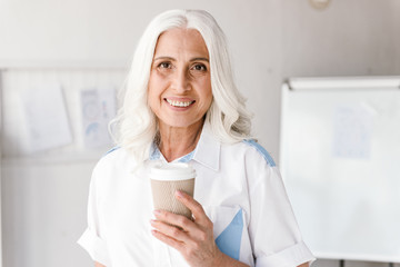 Poster - Mature woman indoors in office working drinking coffee