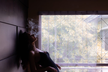 Portrait charming beautiful model woman. Attractive beautiful sexy women is smoking cigarette or weed in dark room at house. Gorgeous woman feels like a dreaming, mind drifting or floating in the air