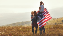 Happy Family With Flag Of America USA At Sunset Outdoors