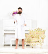 © be free - Full length portrait of a young man in a bathrobe standing isolated in white room with piano. Bearded guy tightening his robe. Sleepy hipster in his apartment
