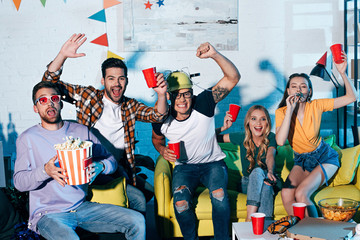 Wall Mural - excited young friends drinking beer and eating snacks at home party