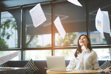 Asian Businesswoman throwing paper after success plan and final project sitting at office near window relaxing freedom concept.