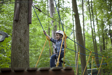 Wall Mural - boy enjoys climbing in the ropes course adventure. smiling child engaged climbing high wire park.