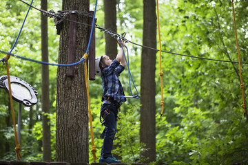 Wall Mural - boy enjoys climbing in the ropes course adventure. smiling child engaged climbing high wire park.