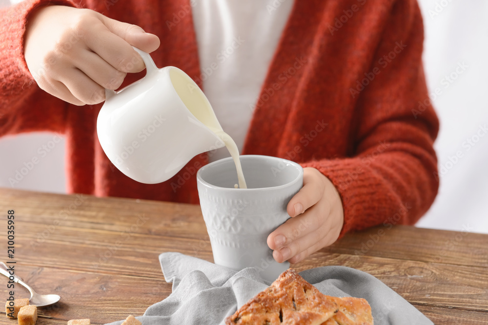 Woman pouring milk into cup of tea on table