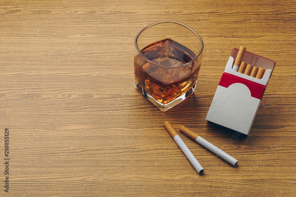 dipping cigarettes in whiskey a glass of bourbon whiskey, two cigarettes with a cigarette pack on the  wooden table Stock Photo