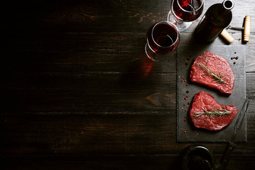 two pieces of fresh meat prepared for frying and wine with glasses on a wooden table