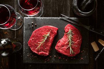 two pieces of fresh meat prepared for frying and wine with glasses on a wooden table