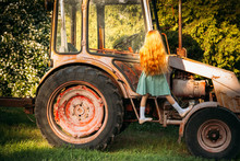 A Little Girl With Red Hair Climbs On The Cab Of A Red Old Tractor