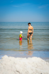 mom and little daughter in a green swimsuit are walking in the water in the sea in the summer