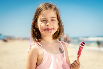 little adorable girl eating a delicious colorful ice cream on the beach in summer