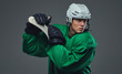 Hockey player wearing green protective gear and white helmet standing with the hockey stick. Isolated on a gray background. 