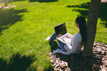Young Successful Businesswoman In Casual Clothes. Woman Sit On Grass Ground, Working On Laptop Pc Computer In City Park On Green Lawn Outdoors On Nature. Mobile Office. Freelance Business Concept.