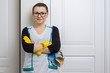 Professional cleaning service. Woman housemaid in yellow rubber gloves with detergents smiling against white doors