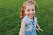 © ViDi Studio - Joyful little cute child baby girl in denim dress walking and running, have fun on green grass lawn in park. Mother, little kid daughter. Mother's Day, love family, parenthood, childhood concept.