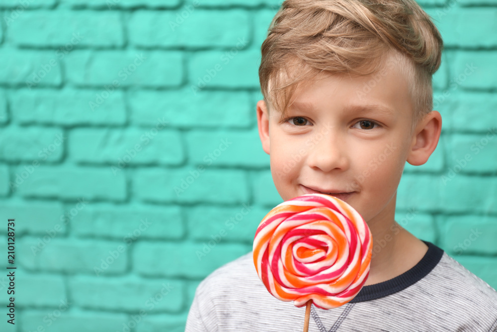Cute little boy with lollipop near color brick wall