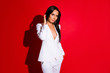 © deagreez - Portrait of cute lovely coquette in white suit with sexy decollete fixing correcting hair looking at camera isolated on vivid red background