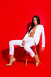 © deagreez - Portrait of tempting horny woman sitting on stool with open jacket wearing on naked body resting relaxing having perfect figure isolated on vivid red background