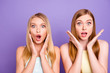 Portrait of shocked frustrated girls with wide open eyes mouth holding palms near cheeks looking at camera isolated on vivid violet background