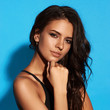 © Dmitry Tsvetkov - Young sexy slim tanned woman in black swimsuit posing against blue background. Closeup Fashion portrait of beautiful girl with long wavy brunette hair. Swimwear or bikini model