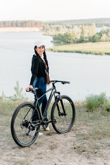 Wall Mural - The beautiful girl is standing by bicycle. Senior woman riding a bike beside a lake. A female biker take a rest after biking