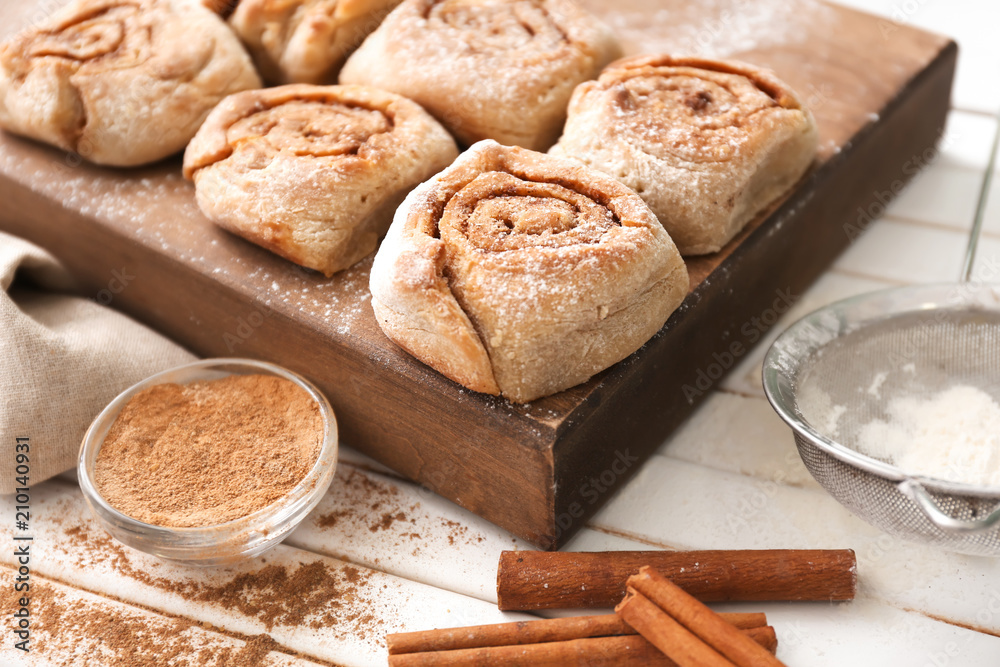 Board with delicious cinnamon buns on wooden background
