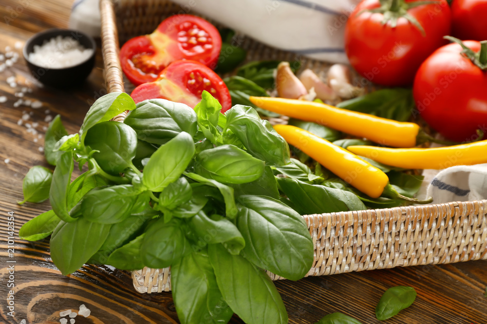 Wicker tray with spices and vegetables on wooden background, closeup