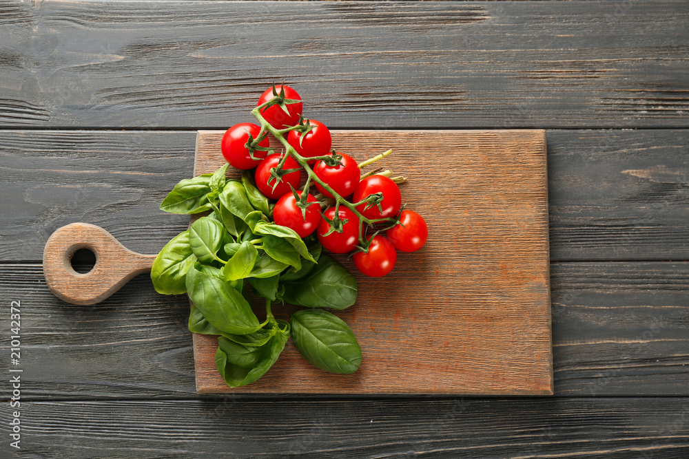 Board with fresh basil and tomatoes on wooden background