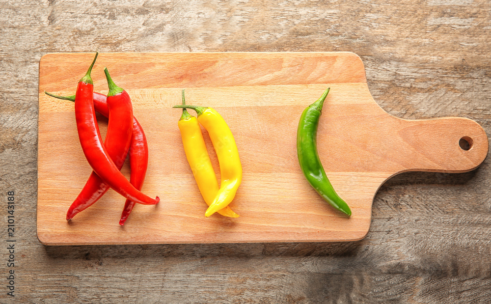 Board with different fresh chili peppers on wooden background