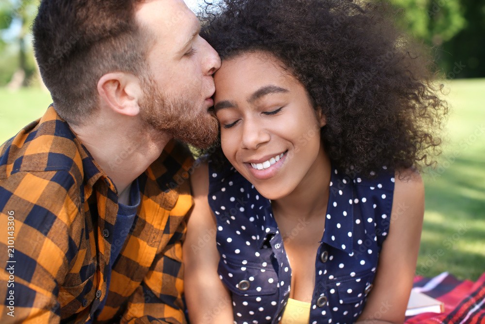 Young loving interracial couple resting in park on spring day