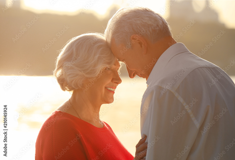 Happy mature couple on riverside at sunset