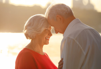 Wall Mural - Happy mature couple on riverside at sunset