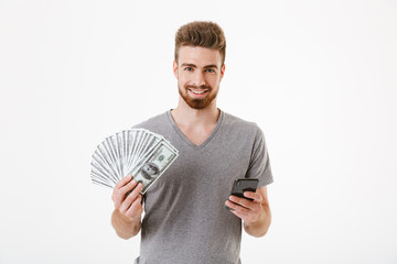 Wall Mural - Man standing isolated using mobile phone holding money. Looking camera.