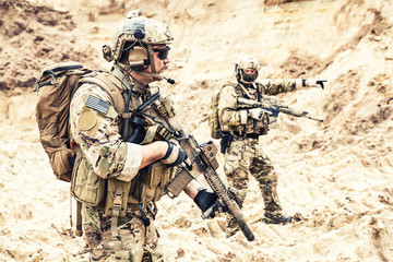 two armed us army commandos or military scouts equipped with radio headset moving forward in sands d