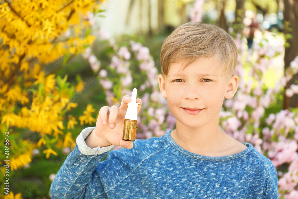 Little boy with nasal drops near blooming tree. Allergy concept