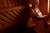 girl in a spa treatment in a traditional sauna with a brush for skin and a washcloth. relaxes wrapped in a white towel