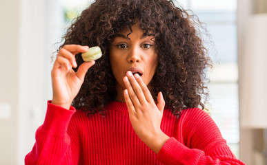 Sticker - African american woman holding macaron cover mouth with hand shocked with shame for mistake, expression of fear, scared in silence, secret concept